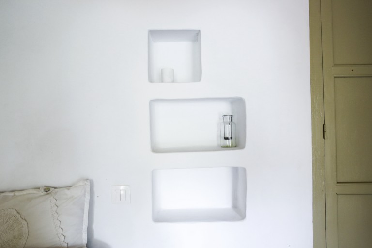 Recessed bedside tables on the wall close to the double bed of Erastos studio with its handmade lace headboard pillows